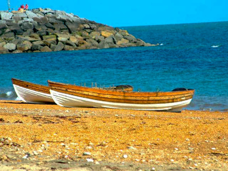 Two wooden fishing boats with brown and white painted hulls beached on golden sand beside turquoise water.