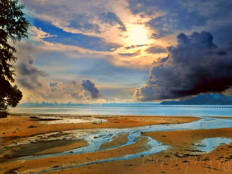 Tropical beach at sunset with tidal channels cutting through sand beneath dramatic clouded sky.