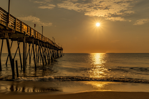 Wooden pier extending into calm ocean waters at golden hour sunset.