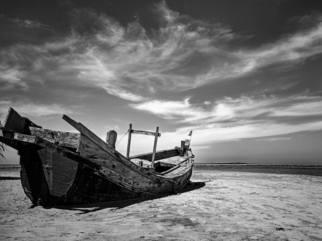 Weathered wooden fishing boat beached on sand with dramatic cloudy sky overhead.