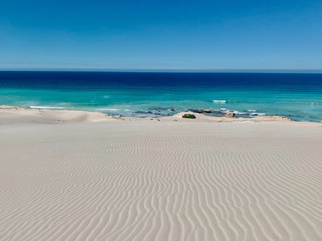 Rippled sand beach stretching toward turquoise ocean under clear blue sky.