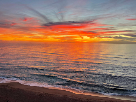 Vibrant sunset over the ocean with dramatic orange and red sky reflecting on calm water and wet sand beach.