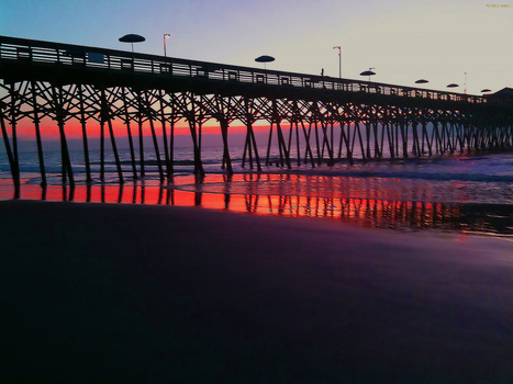 Wooden pier extending into the ocean at sunset, silhouetted against a vibrant pink and purple sky.