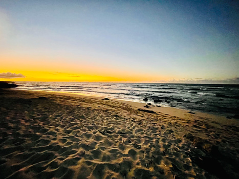 Golden sunrise over ocean with textured wet sand beach in foreground.