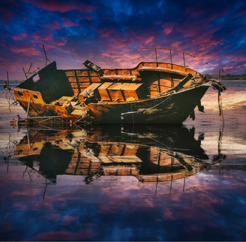 Abandoned wooden fishing boat with golden hull reflected in still water at twilight.