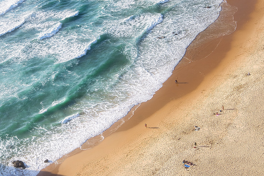 Aerial view of a sandy beach with turquoise waves and scattered beachgoers along the shoreline.