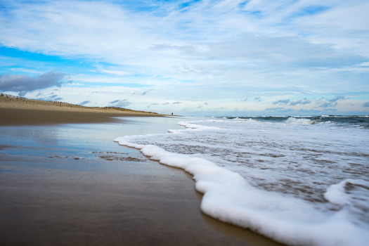 Waves rolling onto a sandy beach with blue sky and clouds at horizon.