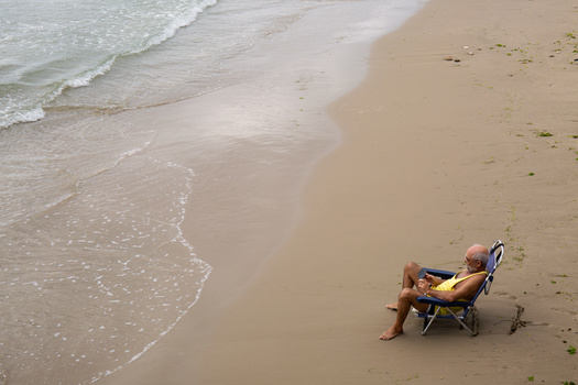 Person relaxing in a beach chair at the shoreline, with gentle waves lapping at the sand.