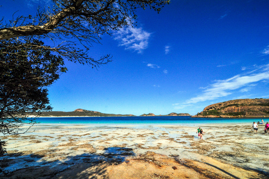 Tropical beach with turquoise water, sandy shore, and rocky headlands under clear blue sky.
