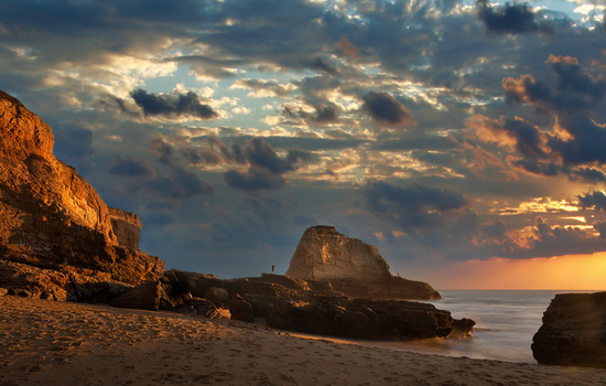 Rocky coastal landscape at golden hour with dramatic clouds and calm ocean water.
