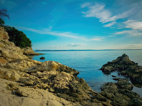 Rocky coastline with turquoise water and small island under clear blue sky.