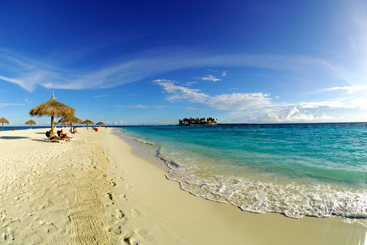 Tropical beach with white sand, turquoise water, and a thatched umbrella shelter under clear blue sky.