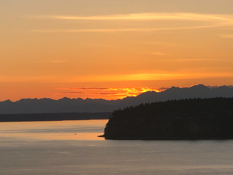 Golden sunset over a calm lake with forested shoreline and distant mountains silhouetted against the sky.