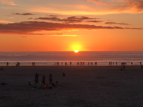 Silhouetted beachgoers watching the sun set over the ocean at dusk.