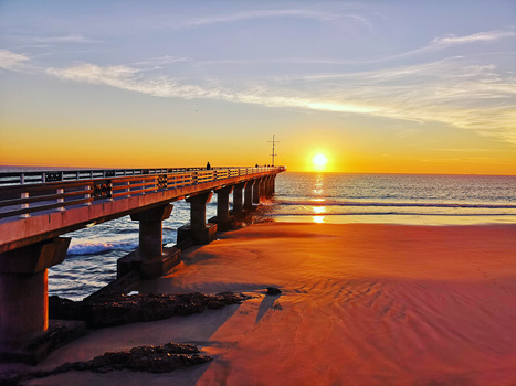 Wooden pier extending into the ocean at sunrise with golden light reflecting on wet sand below.