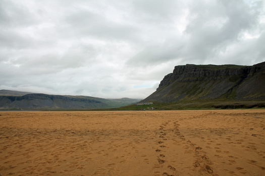 Expansive sandy beach stretching toward dramatic basalt cliffs under overcast sky.