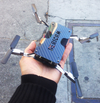 Hand holding a small blue carbon fiber drone frame with yellow and red accents against concrete background.