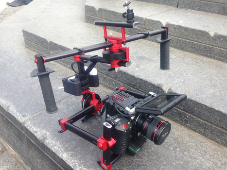 Red and black camera gimbal stabilizer rig mounted on concrete steps with professional video camera attached.