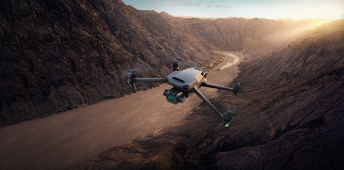 Aerial drone hovering above a canyon with a winding river below and golden sunlight illuminating the rocky landscape.