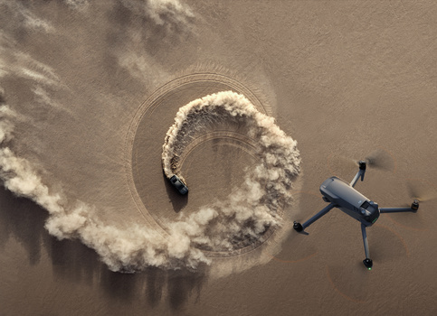 Aerial view of a quadcopter drone alongside a paraglider performing a spiraling maneuver against a brown landscape.