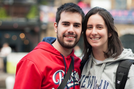 Two smiling people posing together outdoors with a blurred urban background.