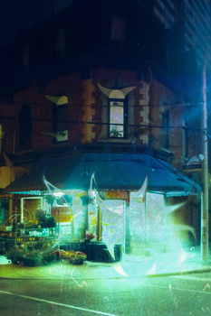 Night photograph of a storefront with neon green lighting and a brick building facade above.