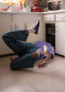 Two people positioned upside-down on a kitchen floor in a playful pose.