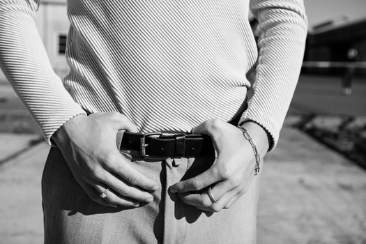 Person's hands adjusting an empty black belt buckle against their torso in black and white photography.
