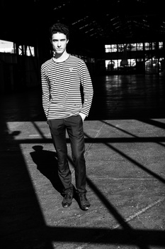 Man in striped shirt walking through industrial space with dramatic window light casting shadows.
