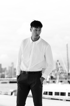 Man in white dress shirt and black trousers standing against urban skyline backdrop.