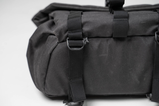 Close-up of a black camera bag with rolled-top closure and D-ring hardware details.