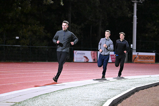 Three runners jogging on a red athletic track at an outdoor sports facility during daytime.