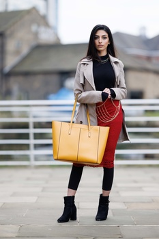 Woman in beige blazer holding yellow and red designer handbags on urban bridge.