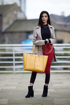 Woman in beige blazer and red pants holding yellow and red handbags on urban rooftop.