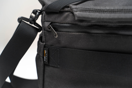 Close-up of a black camera bag's shoulder strap, zipper, and nylon webbing with metal hardware against a white background.