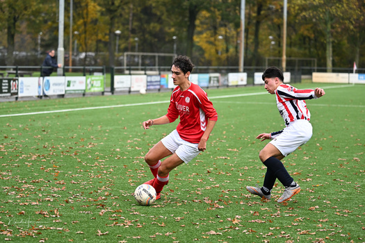 Young soccer player in red jersey controlling ball while opponent in red and white striped jersey defends.