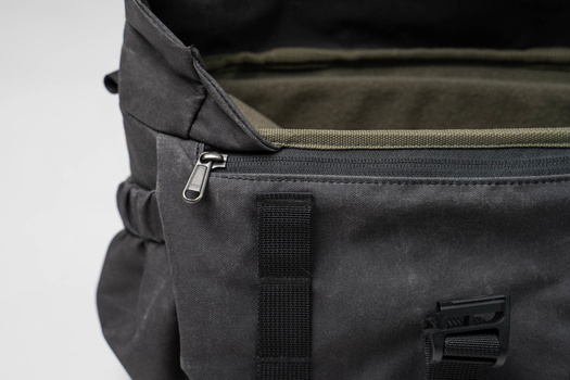 Close-up detail of a dark gray camera bag showing zipper, webbing strap, and fabric texture.