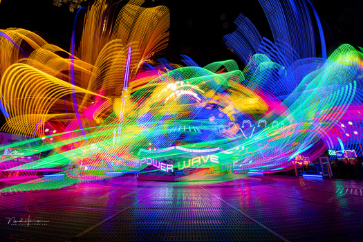 Neon light trails create vibrant flowing streams of magenta, cyan, yellow, and green against a dark background.
