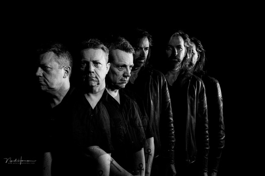 Five men arranged in a line against black background, lit with dramatic side lighting.
