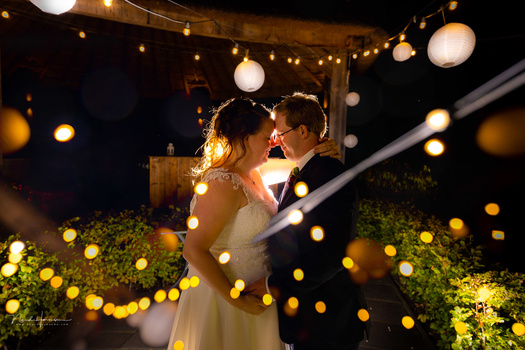 Bride and groom embracing under warm string lights and lanterns at night.