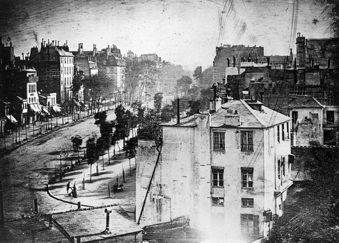 Historical black and white photograph of an urban street with classical architecture and period buildings.