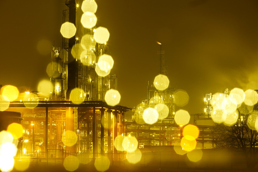 Industrial refinery complex at night with bokeh lights creating warm golden halos throughout the composition.