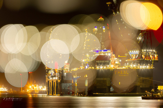 Illuminated waterfront buildings at night with bokeh light circles in foreground.