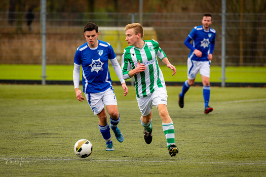 Young soccer players in blue and green striped jerseys competing for the ball during a match on grass.