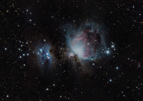 The Orion Nebula complex showing blue and reddish emission nebulae with dark dust lanes and bright stars.