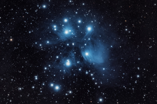 The Pleiades star cluster featuring bright blue stars surrounded by nebulosity against a dark starfield.