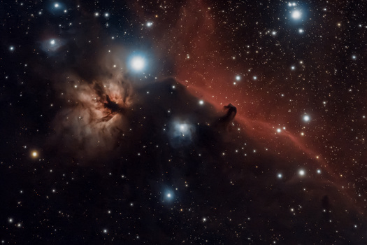 Deep-space photograph showing a reflection nebula with dark dust clouds silhouetted against glowing red and brown gas, surrounded by bright stars.