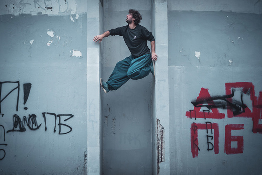 Parkour athlete jumping horizontally between two concrete pillars in an urban stairwell with graffiti.