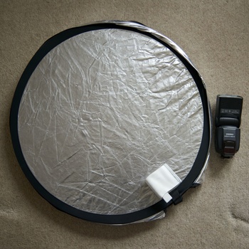 Circular reflector with silver and black surfaces next to a camera flash unit on tan carpet.