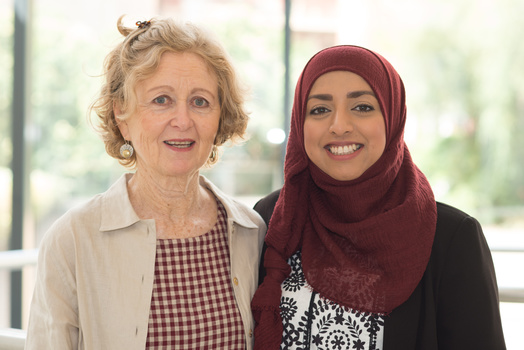 Two women smiling at the camera in a bright interior space with natural window lighting.